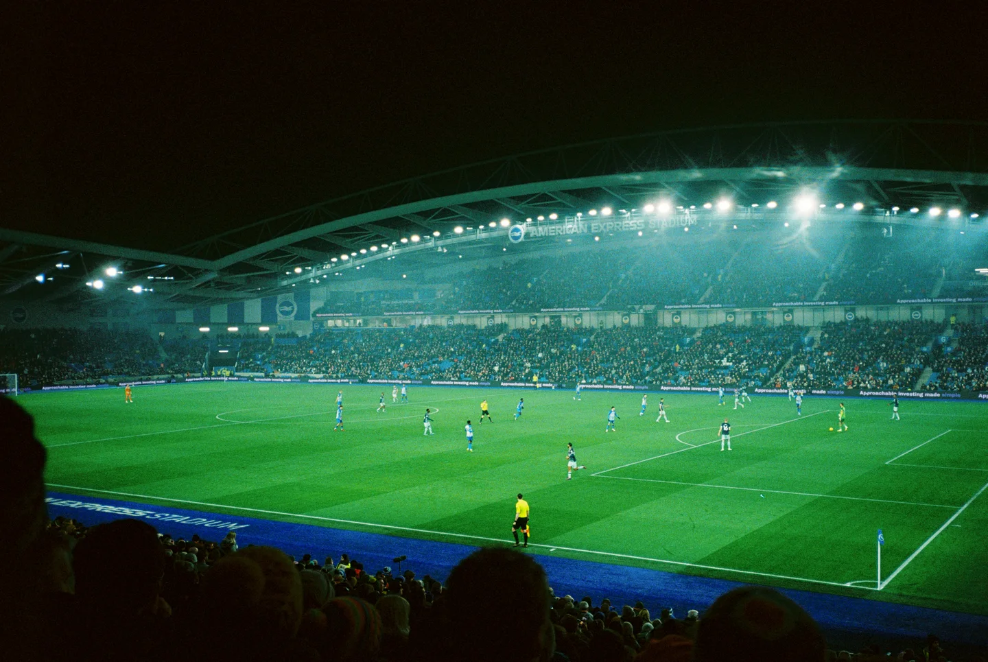 Spectators watching an evening football match in a brightly lit stadium